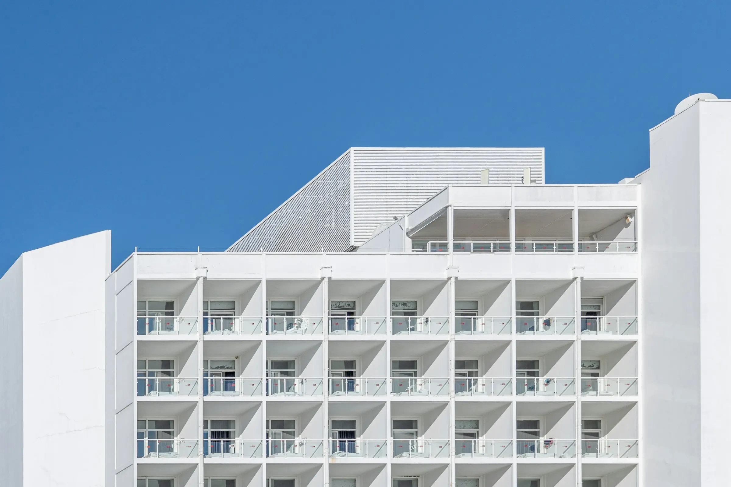 Weißes Wohngebäude mit Balkonen vor blauem Himmel