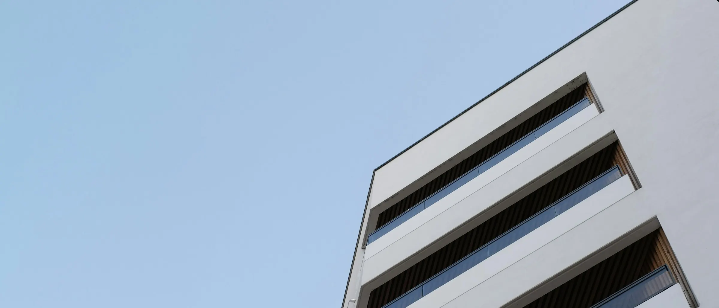 Weißes Wohnhaus mit Balkonbändern vor hellem Himmel