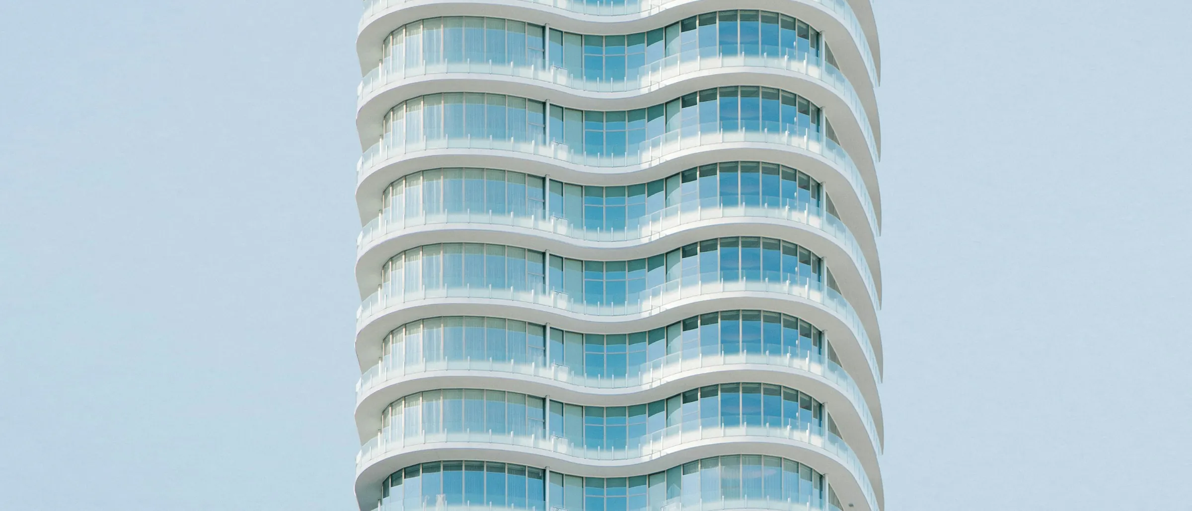 Weißer Wohnturm mit geschwungenen Glasfronten vor hellem Himmel